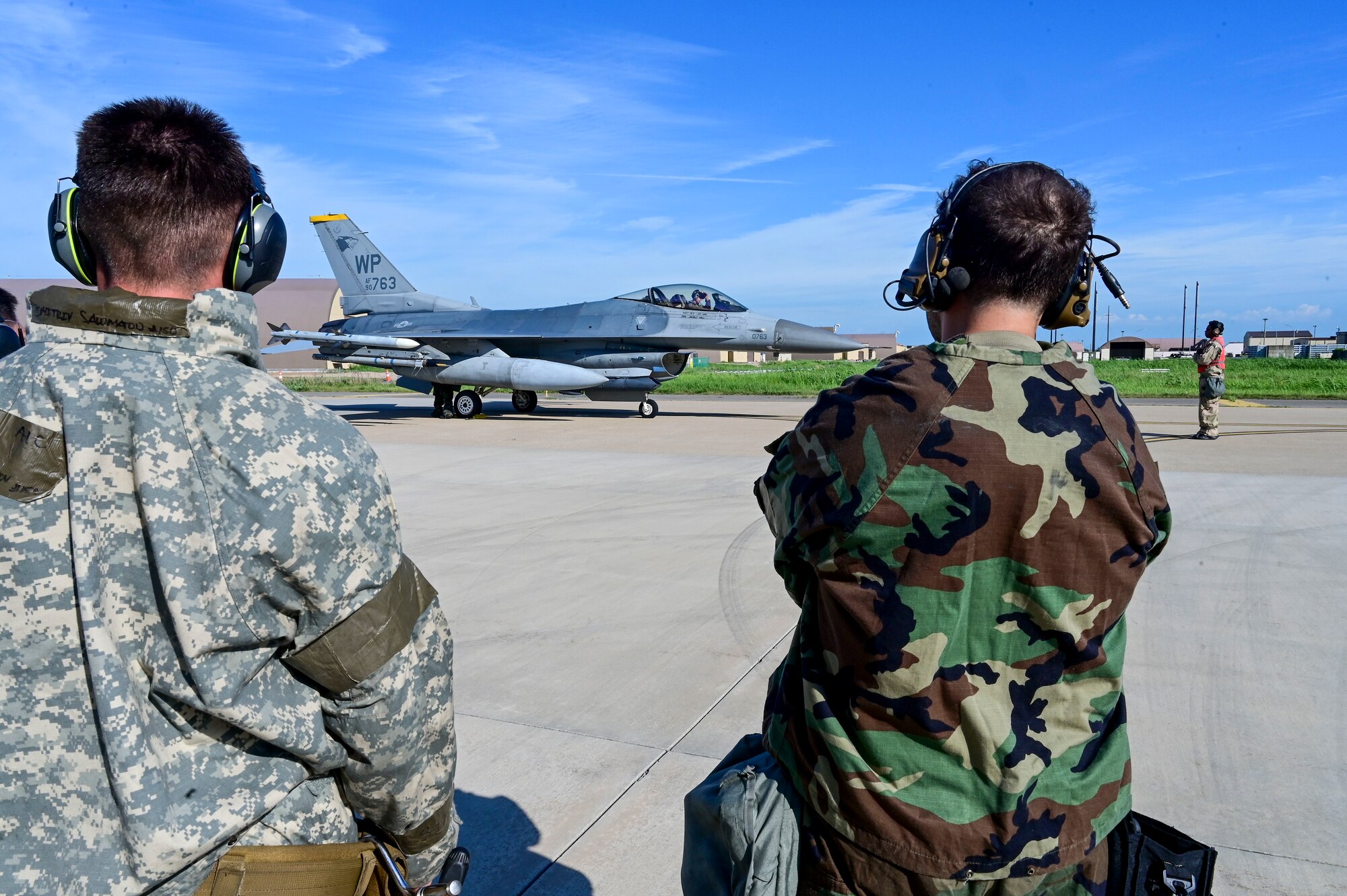 Two men look at a jet in the distance.