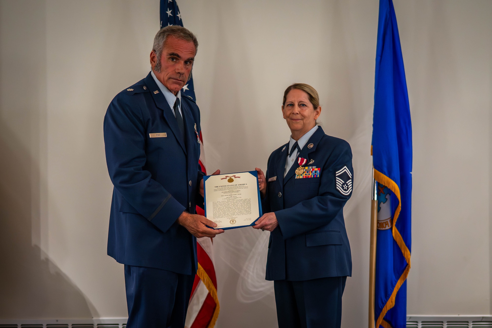 Two people stand together on stage holding a retirement certificate.