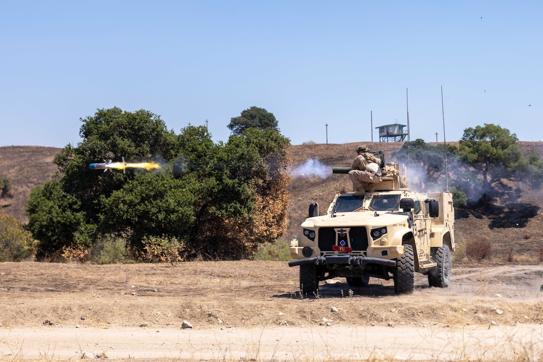 A Marine fires a missile from atop a vehicle in a field during the day.