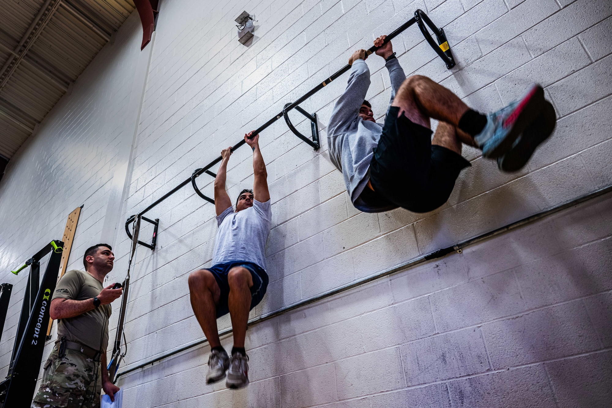 Military members in physical training gear perform a physical challenge in a gym.