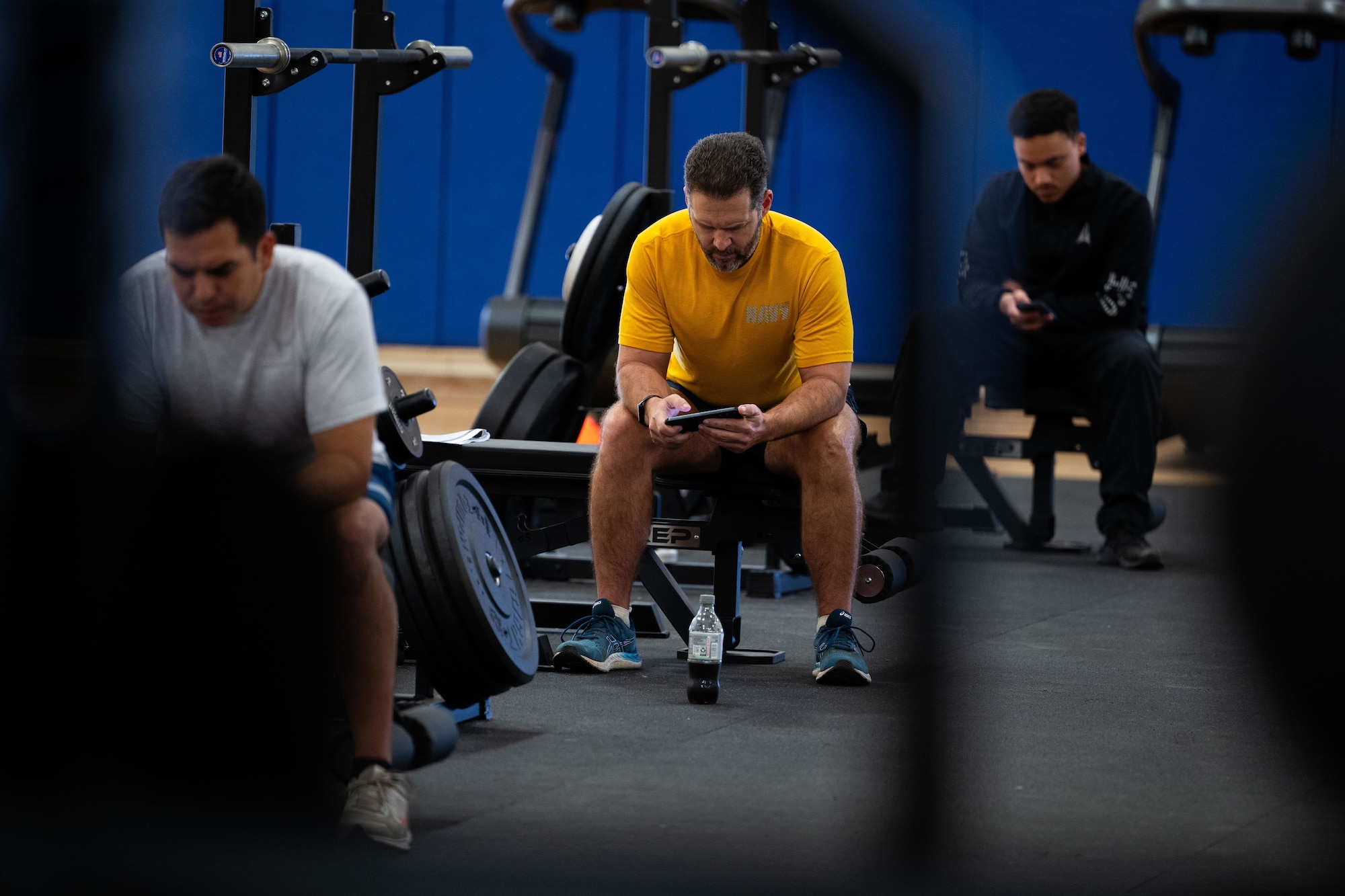 Military members in physical training gear use their phones for a cognitive challenge in a gym.