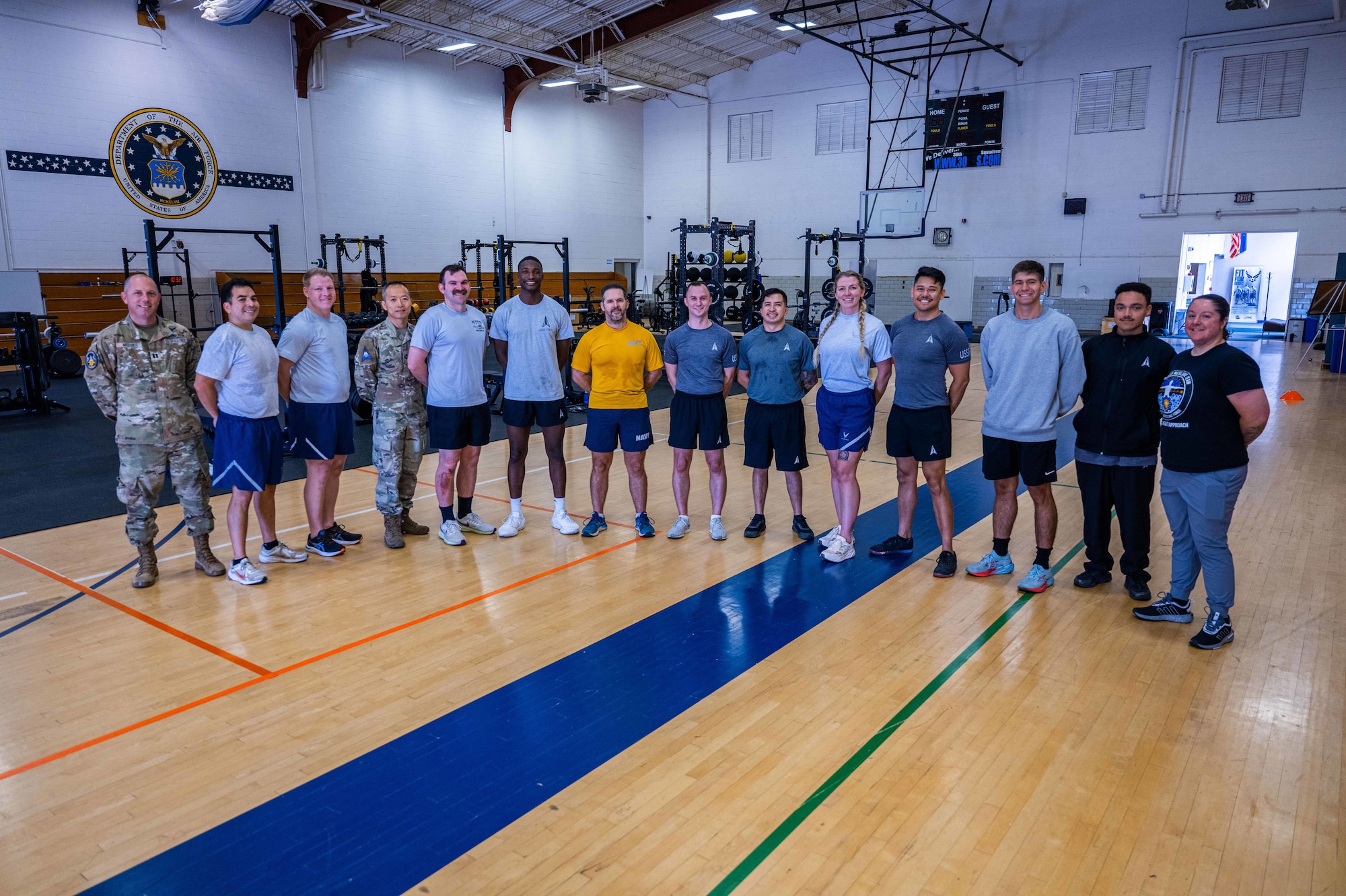 a group of 14 people stand shoulder-to-shoulder in a gym.