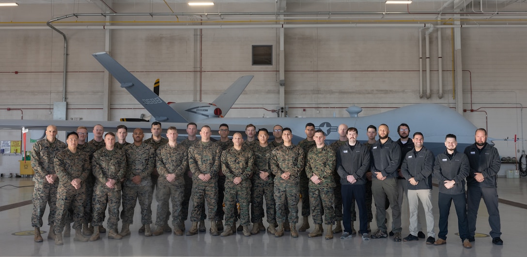 The first classes of MQ-9A Reaper mechanics and technicians, the instructors, and Center for Naval Aviation Technical Training Unit Cherry Point leaders stand for a group photo at the Marine Unmanned Aerial Vehicle Training Squadron 2, 2nd Marine Aircraft Wing, hangar, Marine Corps Air Station Cherry Point, North Carolina, Dec. 12, 2024.