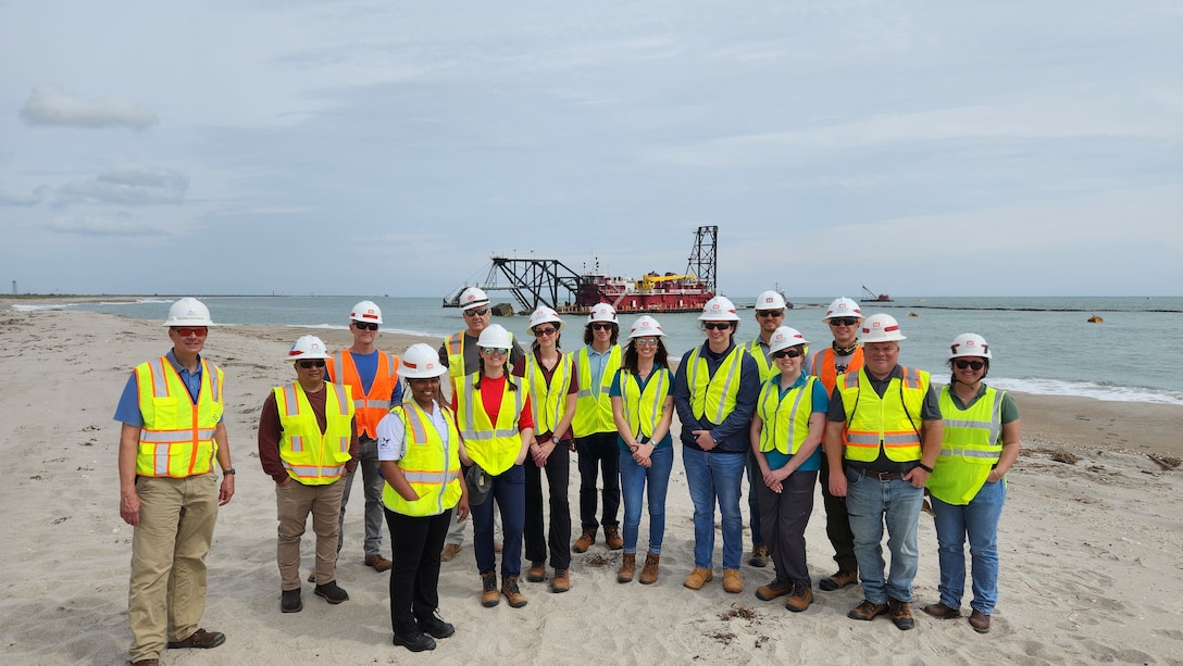 Members from the USACE Canaveral Sand Bypass project delivery team (PDT) stand beside non-Federal sponsor representative Bob Musser from Canaveral Port Authority, for a group photo on the shorelines of Port Canaveral.