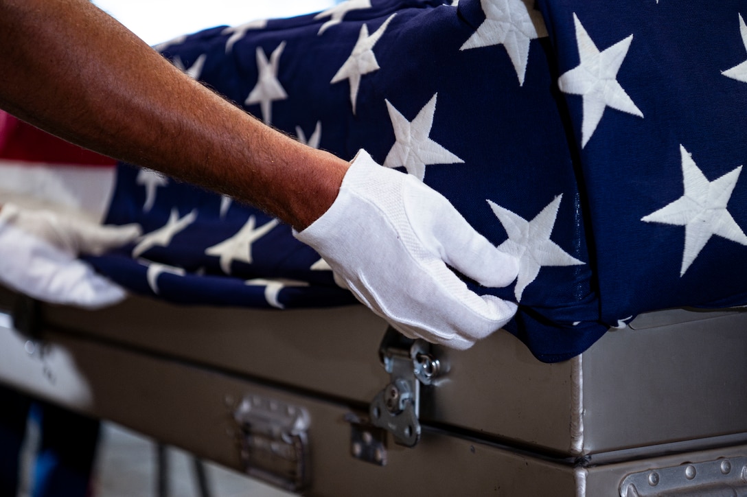 U.S. Navy Chief Petty Officer Alexander Greenspan, an explosive ordnance disposal technician assigned to the Defense POW/MIA Accounting Agency, secures the American flag to a casket holding potential remains during a repatriation ceremony in Da Nang Province, Vietnam, July 25, 2025.