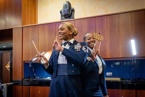 Two U.S. Air Force women smile while holding props for a photo.