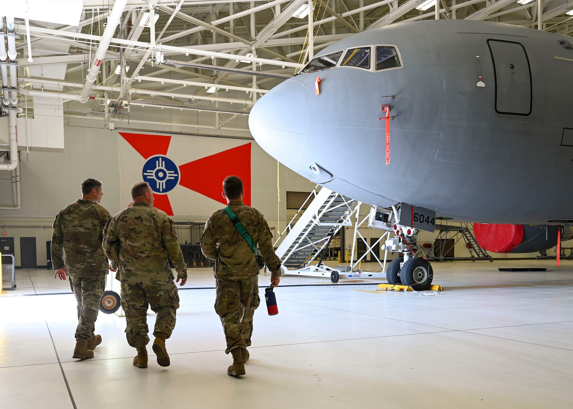 Three men in military unforms walk walk next to a large military plane.