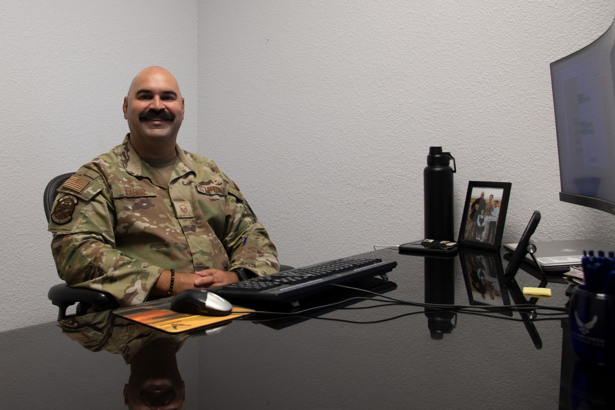 Master Sgt. Tabor smiles at the camera while sitting at his desk.