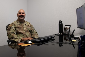 Master Sgt. Tabor smiles at the camera while sitting at his desk.