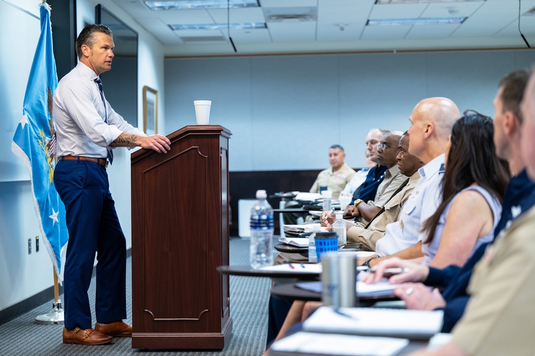 A side view of the defense secretary standing at a podium speaking to seated general officers in a classroom.