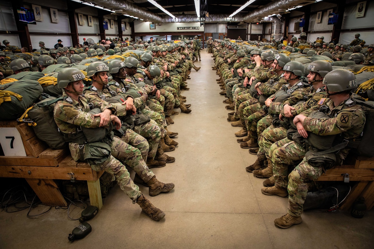 Service members in parachute gear sit inside an aircraft.