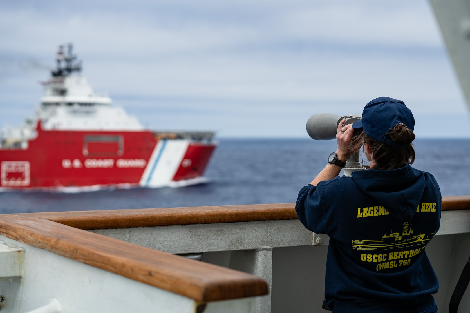 U.S. Coast Guard Cmdr. Caitlin Clemons, Executive Officer of the Coast Guard Cutter Bertholf (WMSL 750), looks through a set of binoculars at Coast Guard Cutter Storis (WAGB 21) in the Pacific Ocean, June 29, 2025. Bertholf is the first of the Coast Guard’s Legend-class National Security Cutters, while Storis is the Coast Guard’s most recently acquired ice breaker. (U.S. Coast Guard photo by Petty Officer 3rd Class Avery Tibbets)
