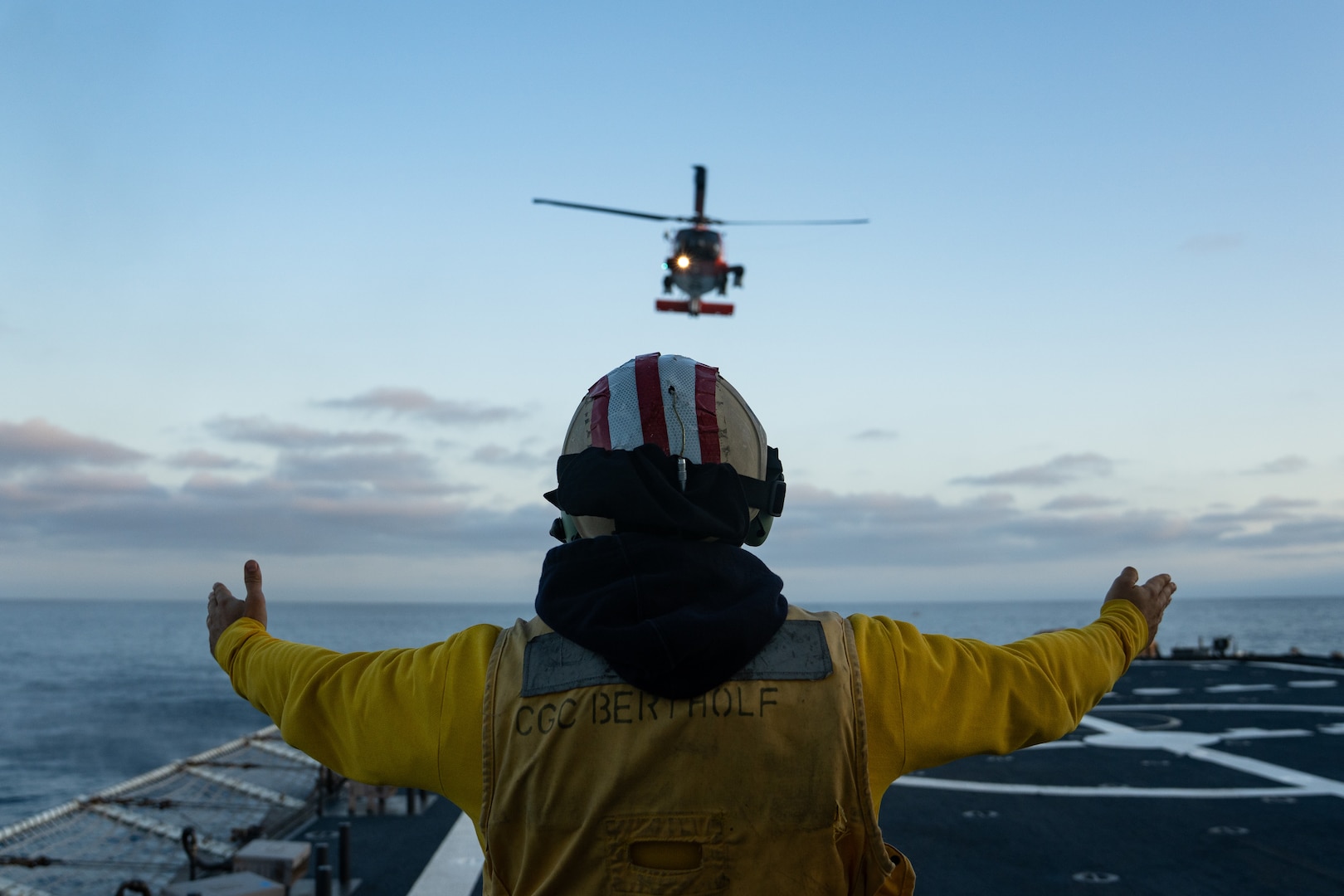 U.S. Coast Guard Lt. Drew LoVullo, a landing signals officer aboard the U.S. Coast Guard Cutter Bertholf (WMSL 750), directs an MH-60 Jayhawk helicopter from Air Station San Diego during flight operations in the Pacific Ocean, June 25, 2025. Training is essential to maintaining unit readiness and proficiency for Bertholf and the local air stations. (U.S. Coast Guard photo by Petty Officer 3rd Class Avery Tibbets)