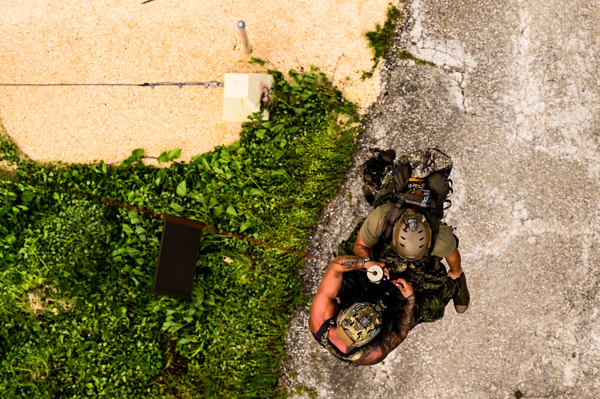 Two U.S. Air Force Airmen from the 563rd Rescue Group are hoisted up to an HH-60W Jolly Green II helicopter after receiving jungle training during exercise Resolute Force Pacific in Tinian, Northern Mariana Islands, July 23, 2025. REFORPAC is part of the first-in-a-generation Department-Level Exercise series, designed to deliver combat airpower to the Indo-Pacific region at speed and scale, and conduct operations in a contested, dynamic environment. (U.S. Air Force photo by Senior Airman Andrew Garavito)