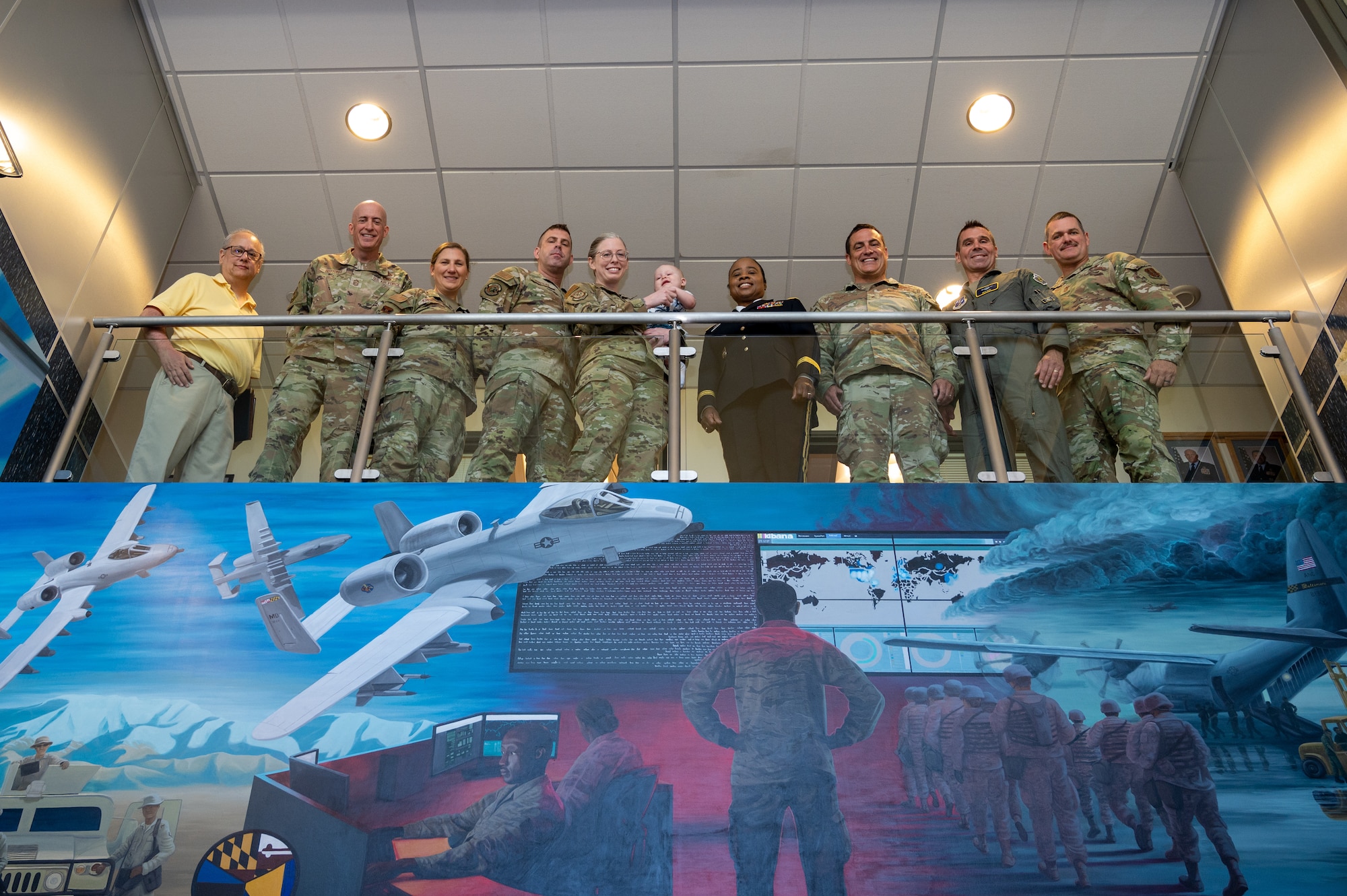 Leadership of the Maryland National Guard and Maryland Air National Guard Staff Sgt. Rachel Underwood, public affairs specialist for the 175th Wing, and family, pose for a group photo after a mural recognition ceremony in the headquarters building at Warfield Air National Guard Base at Martin State Airport, Maryland, August 10, 2025. Underwood was recognized during the ceremony for painting the three-panel acrylic mural, two panels spanning 14.5 feet by 8 feet, and a center panel of 16.5 feet by 6 feet, over the course of a year in order to tell the story of the Maryland Air National Guard and to be hung at the entrance of the 175th Wing headquarters' building. (U.S. Air National Guard Photo by Staff Sgt. Julian Kemper)