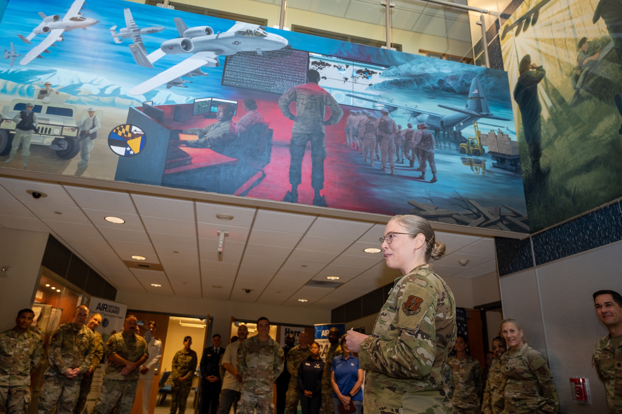 Maryland Air National Guard Staff Sgt. Rachel Underwood, public affairs specialist for the 175th Wing, speaks to attendees of the mural recognition ceremony in the headquarters building at Warfield Air National Guard Base at Martin State Airport, Maryland, August 10, 2025. Underwood was recognized during the ceremony for painting the three-panel acrylic mural, two panels spanning 14.5 feet by 8 feet, and a center panel of 16.5 feet by 6 feet, over the course of a year in order to tell the story of the Maryland Air National Guard and to be hung at the entrance of the 175th Wing headquarters' building. (U.S. Air National Guard Photo by Staff Sgt. Julian Kemper)