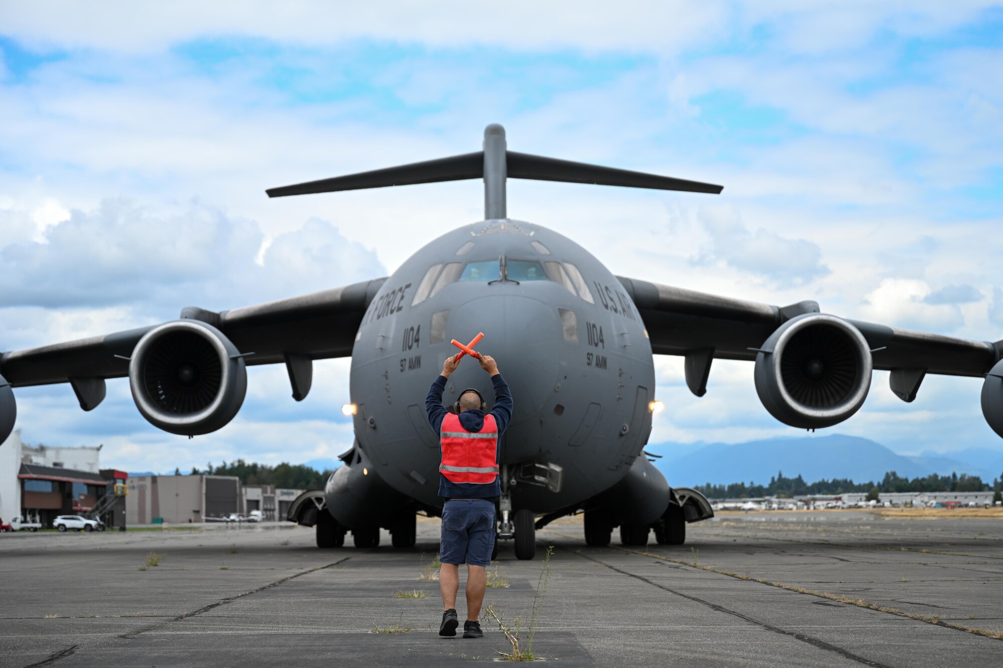 Johnny Garcia, 97th Aircraft Maintenance Squadron C-17 Globemaster III aircraft crew chief, marshals a C-17 onto the flightline of the Abbotsford International Airport, Canada, Aug. 8, 2025. The Altus Air Force Base Demonstration Team arrived in Canada for the Abbotsford International Air Show to showcase a small part of the 97th Air Mobility Wing mission with an aerial refueling demonstration. (U.S. Air Force photo by Airman 1st Class Lauren Torres)