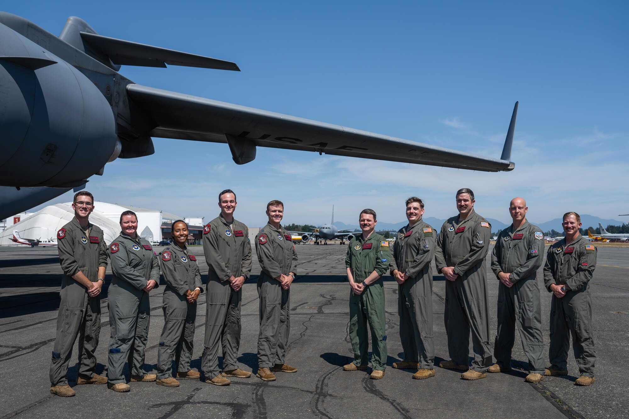 Airmen assigned to the 97th Air Mobility Wing pose for a photo under the wing of a C-17 Globemaster III aircraft at the Abbotsford International Airport, Canada, Aug.10, 2025. The C-17 crew is to the left of the photo and the KC-46 crew is to the right, both teams performed at the Abbotsford International Air Show. (U.S. Air Force photo by Airman 1st Class Lauren Torres)