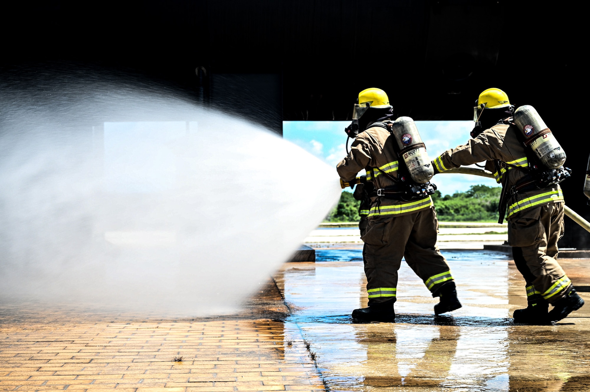 A U.S. Air Force Airman from the 11th Combat Air Base Squadron and a firefighter from the Saipan International Airport Aircraft Rescue and Firefighting Department redirect the flow of water from a fire hose nozzle during exercise Resolute Force Pacific in Saipan, Northern Mariana Islands, July 17, 2025. REFORPAC is part of the first-in-a-generation Department-Level Exercise series, designed to deliver combat airpower to the Indo-Pacific region at speed and scale, and conduct operations in a contested, dynamic environment. (U.S. Air Force photo by Senior Airman Andrew Garavito)