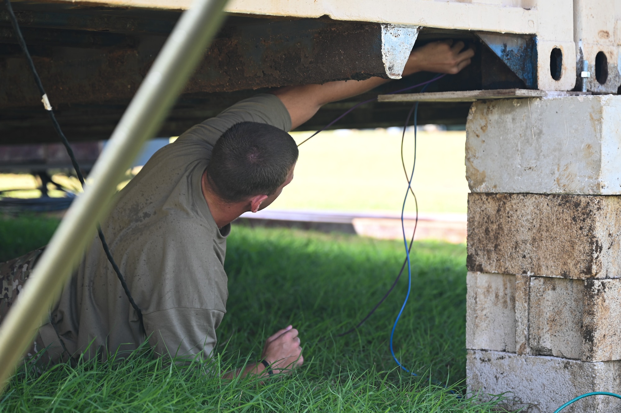 A U.S. Air Force Airman from the 11th Combat Air Base Squadron runs an ethernet cable underneath a trailer at the 11th Air Task Force site in Saipan, Northern Mariana Islands, July 16, 2025, during exercise Resolute Force Pacific. REFORPAC is designed to deliver Air Force capabilities to the Indo-Pacific region at speed and scale, and conduct operations in a contested, dynamic environment. (U.S. Air Force photo by Senior Airman Andrew Garavito)