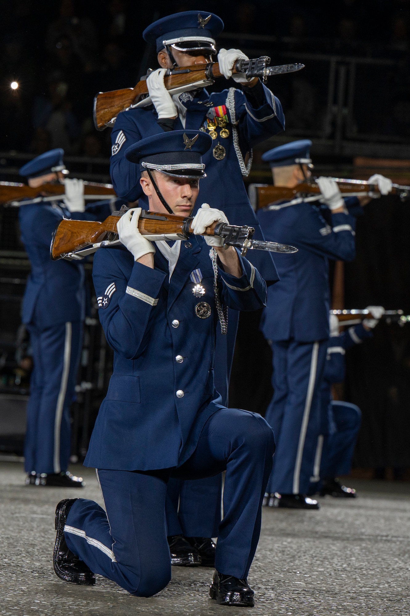 U.S. Air Force Senior Airman Crìsdean James Langan, kneeling center, ceremonial guardsman with the U.S. Air Force Honor Guard Drill Team, conducts a kneeling-bone-crusher drill movement during a performance of the 75th Royal Edinburgh Military Tattoo in Edinburgh, Scotland, Aug. 1, 2025. Military bands and drill teams from the U.S., United Kingdom, Switzerland, Canada, Germany, Poland, and Ukraine performed during the 24-day event. (U.S. Air Force photo by Hayden Hallman)