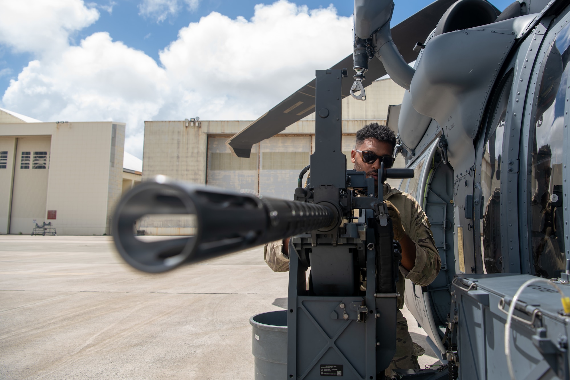 point of view of a machine gun barrel mounted to the side of a helicopter and a military member inspecting behind it