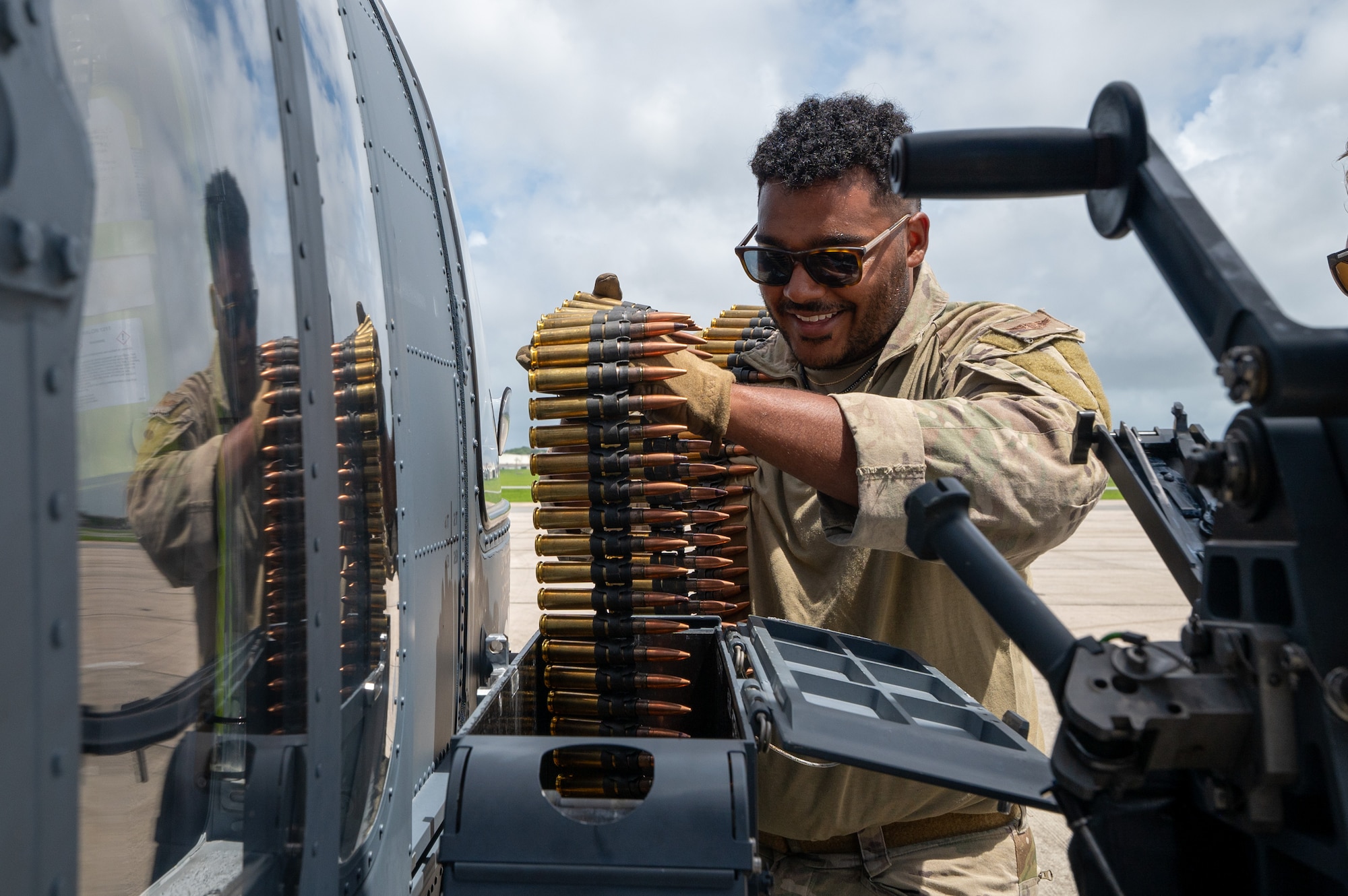 military member holds ammunition for a mounted weapon on the side of a helicopter