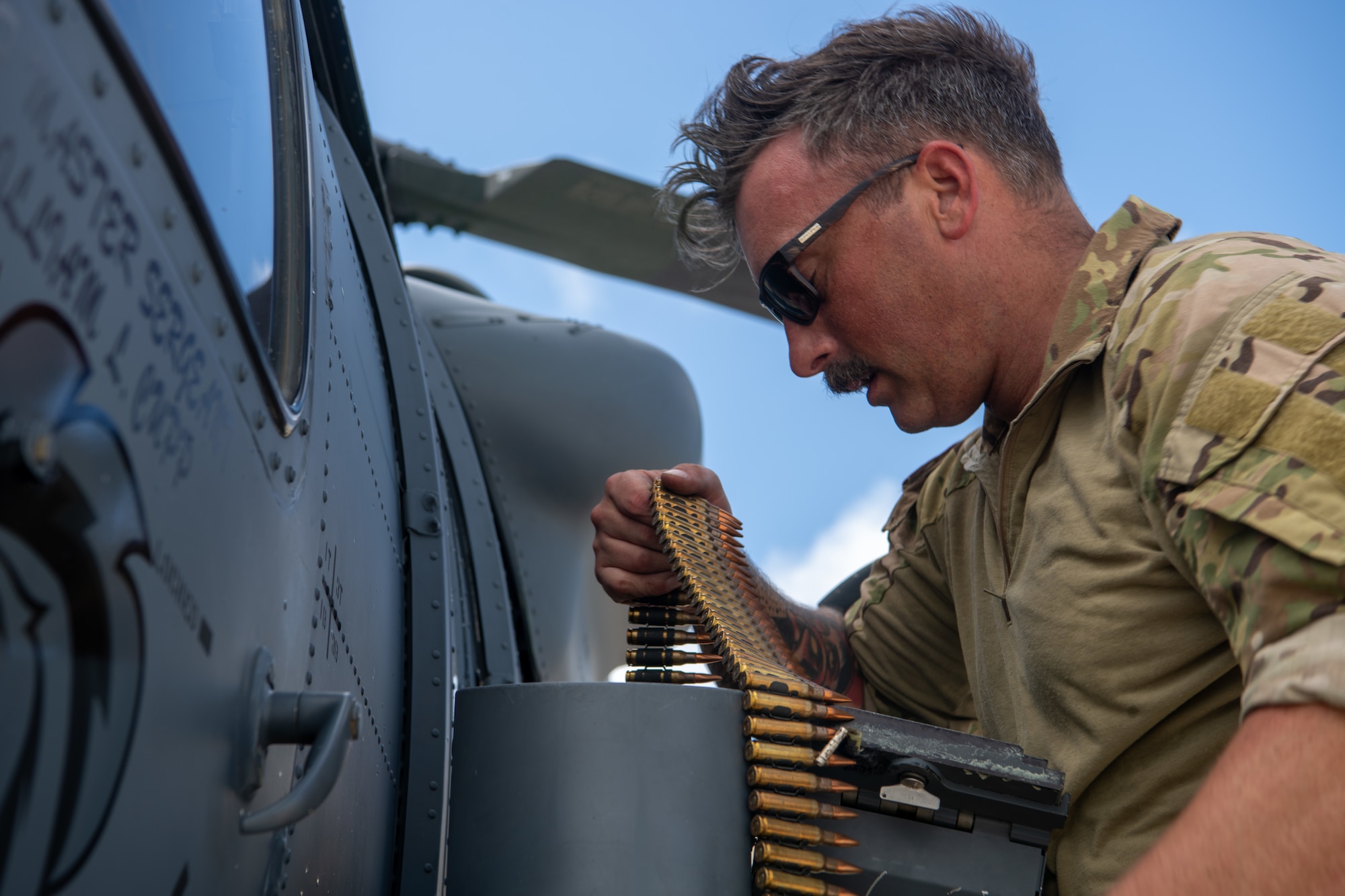 military member holds ammunition for a mounted weapon on the side of a helicopter