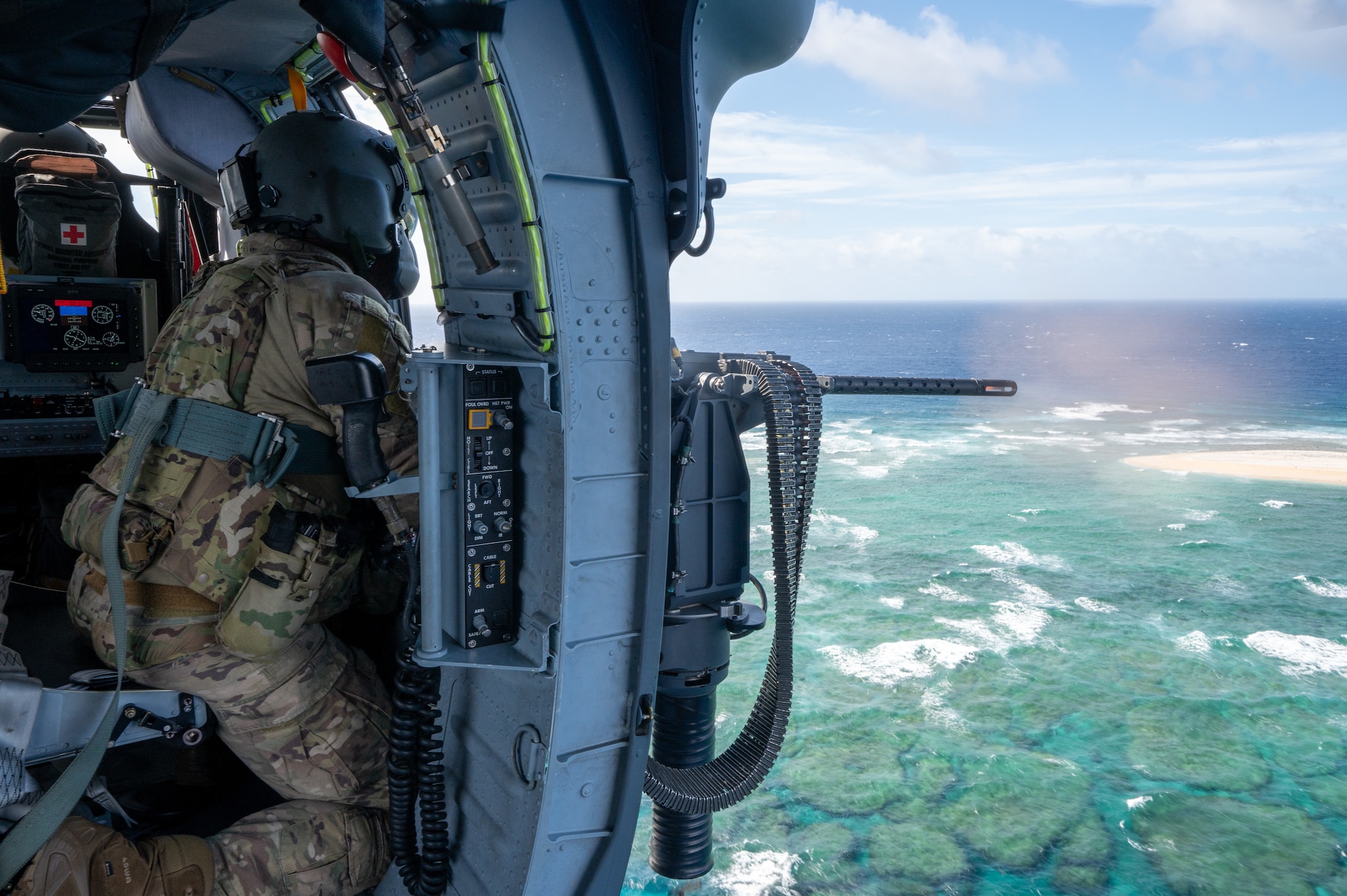 a military member sits in a helicopter while controlling a mounted machine gun with a smoke cloud shows the explosion