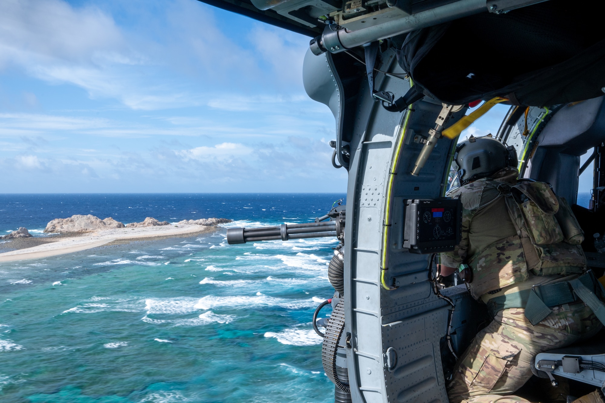a military member sits in a helicopter while controlling a mounted minigun
