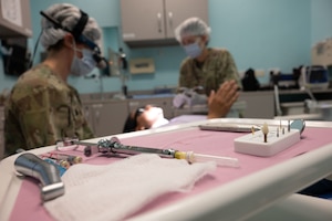 A syringe lays on a treatment table as U.S. Air Force Lt. Col. Melissa Thomas, left,  379th Expeditionary Medical Squadron dentist, and Senior Airman Noemi Kahlia, 379th EMDS dental technician, listen to a patient within the U.S. Central Command area of responsibility, Aug. 8, 2025. The 379th EMDS Dental Office provides care for the entire base, including international mission partners. (U.S. Air Force photo by Senior Airman Dieondiere Jefferies)