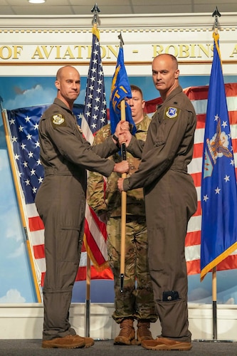 two airmen look at the camera while holding a guidon