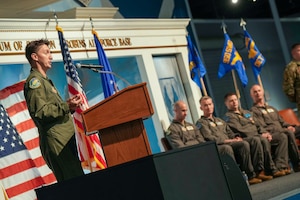 an airman speaks from behind a podium as four others look on