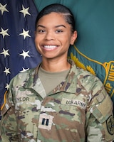Woman in U.S. Army uniform standing in front of two flags.
