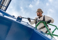 Romeo Aquino, painter, Code 730, Crane Maintenance, works high above the shipyard while repainting Portal Crane 92, July 31, 2025, at Puget Sound Naval Shipyard & Intermediate Maintenance Facility in Bremerton, Washington. A team of painters from Code 730 has spent the better part of the summer updating cranes 80, 82 and 92. The paints used are silicone alkyd enamel, adding a higher gloss sheen for ease of cleaning purposes, for better UV deflection which also helps slow the oxidation process down. (U.S. Navy photo by Wendy Hallmark)