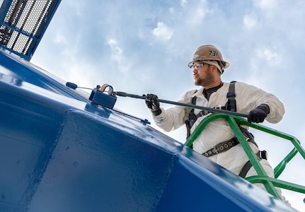 Romeo Aquino, painter, Code 730, Crane Maintenance, works high above the shipyard while repainting Portal Crane 92, July 31, 2025, at Puget Sound Naval Shipyard & Intermediate Maintenance Facility in Bremerton, Washington. A team of painters from Code 730 has spent the better part of the summer updating cranes 80, 82 and 92. The paints used are silicone alkyd enamel, adding a higher gloss sheen for ease of cleaning purposes, for better UV deflection which also helps slow the oxidation process down. (U.S. Navy photo by Wendy Hallmark)