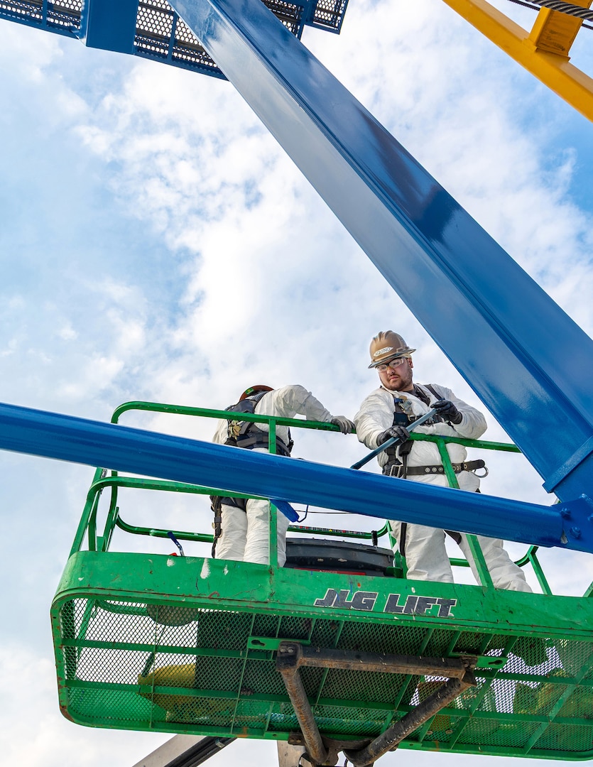 Romeo Aquino, painter, and Darius Aldan, work lead, Code 730, Crane Maintenance, work side-by-side on one of three newly painted portal cranes at July 31, 2025, at Puget Sound Naval Shipyard & Intermediate Maintenance Facility in Bremerton, Washington. (U.S. Navy photo by Wendy Hallmark)