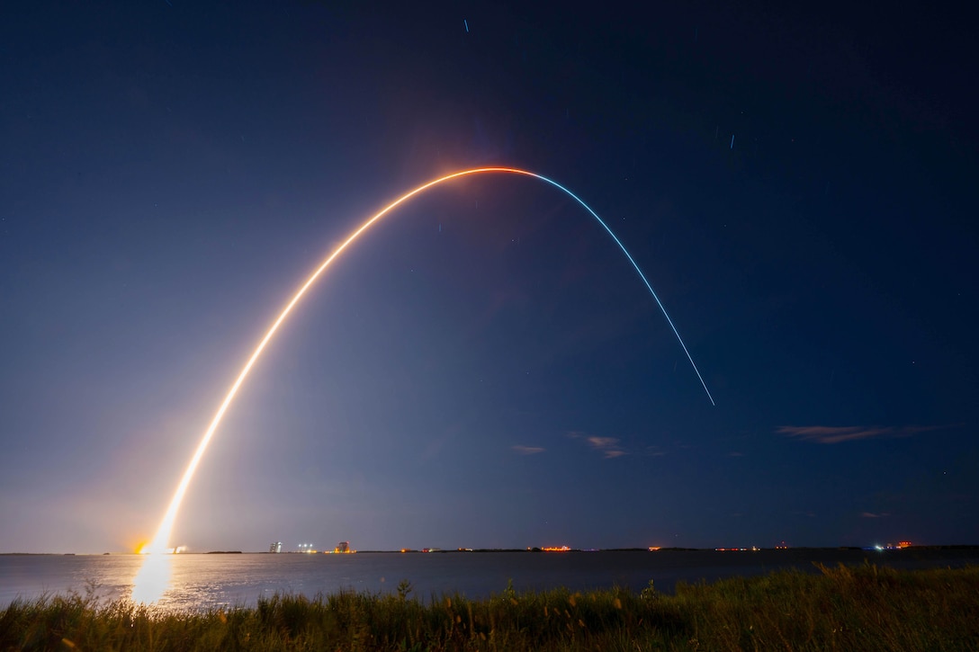 A rocket launches into a deep blue sky leaving a bright orangish streak.