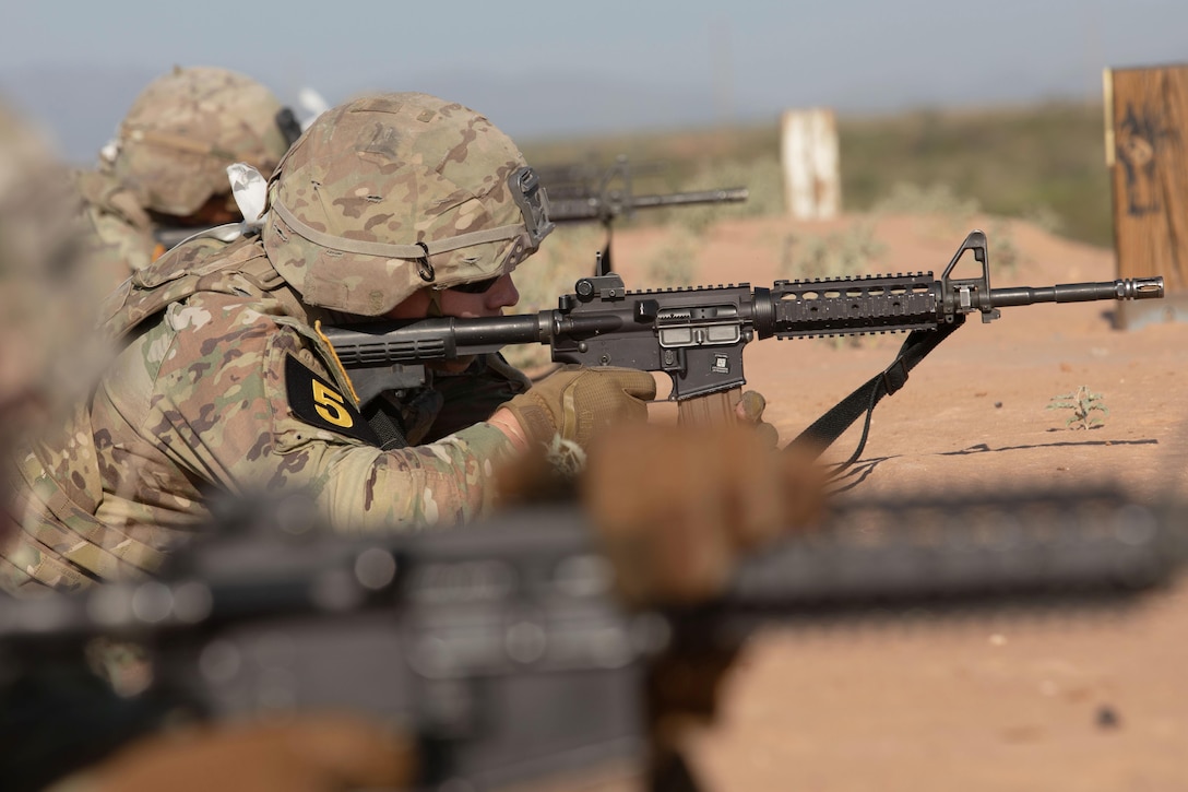 A close-up of a soldier laying in the dirt firing a weapon.