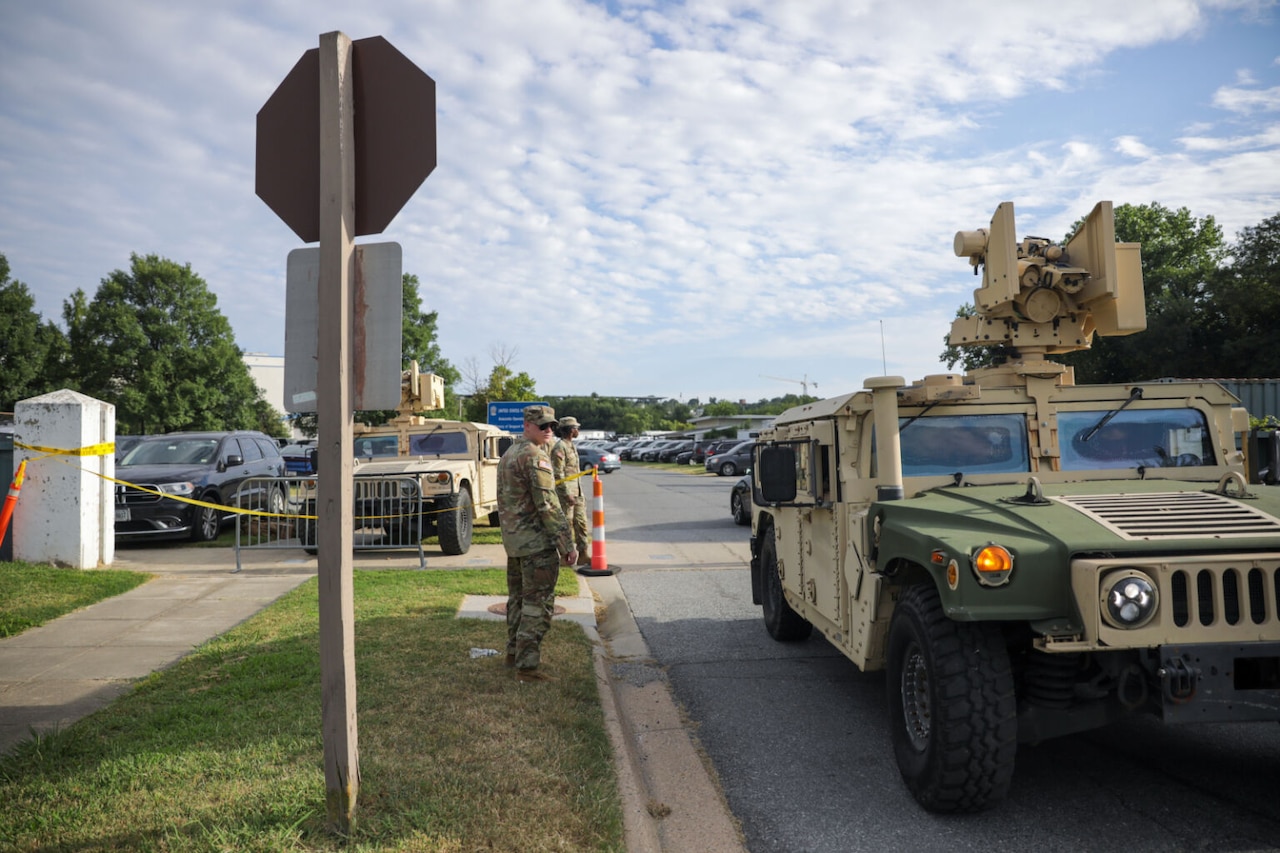 Military personnel stand near a military vehicle.