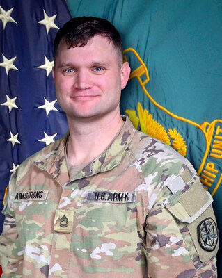 Man in U.S. Army uniform standing in front of two flags.