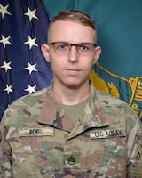 Man in U.S. Army uniform standing in front of two flags.