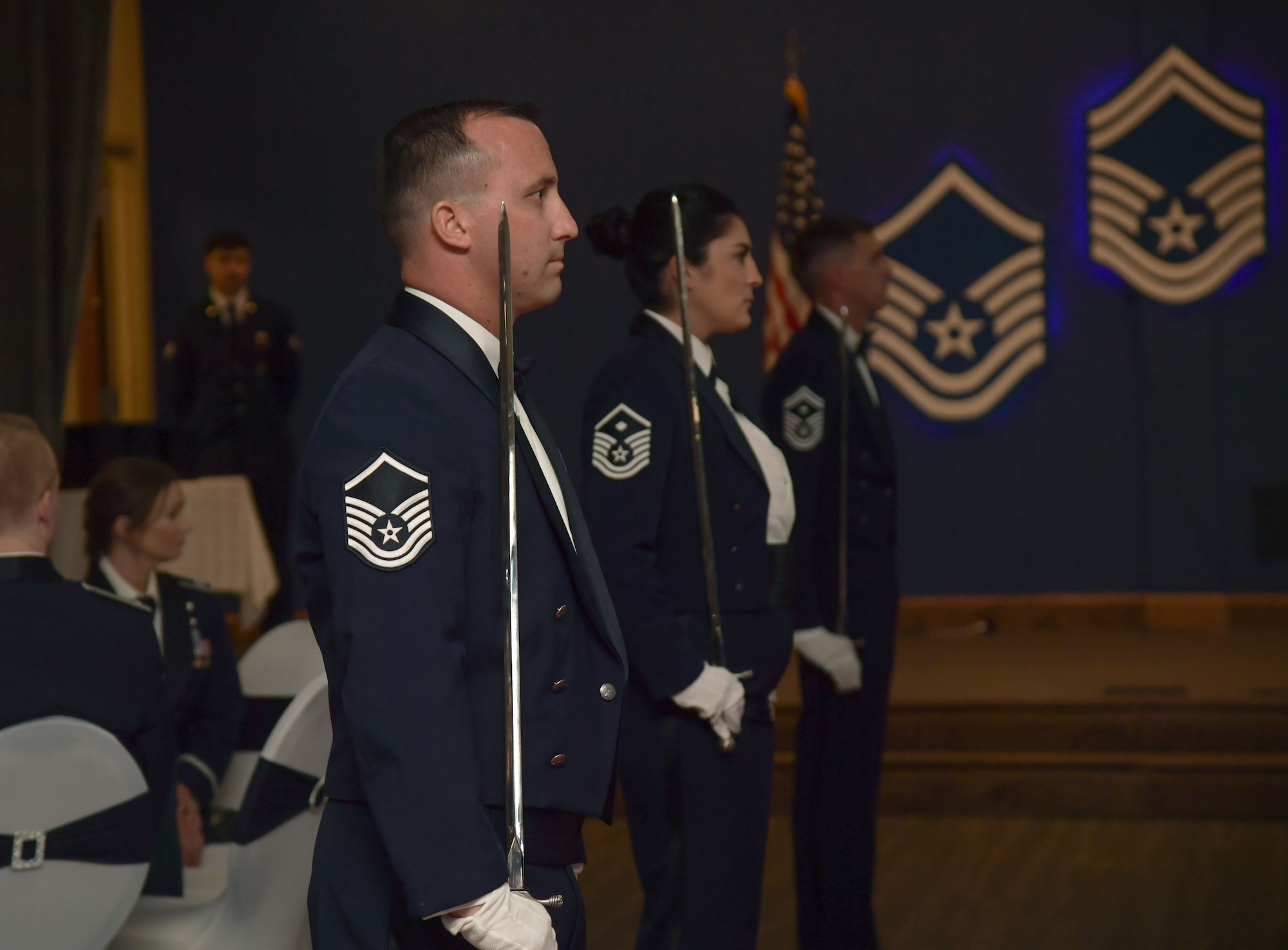People wearing military uniforms hold saber swords while standing at attention