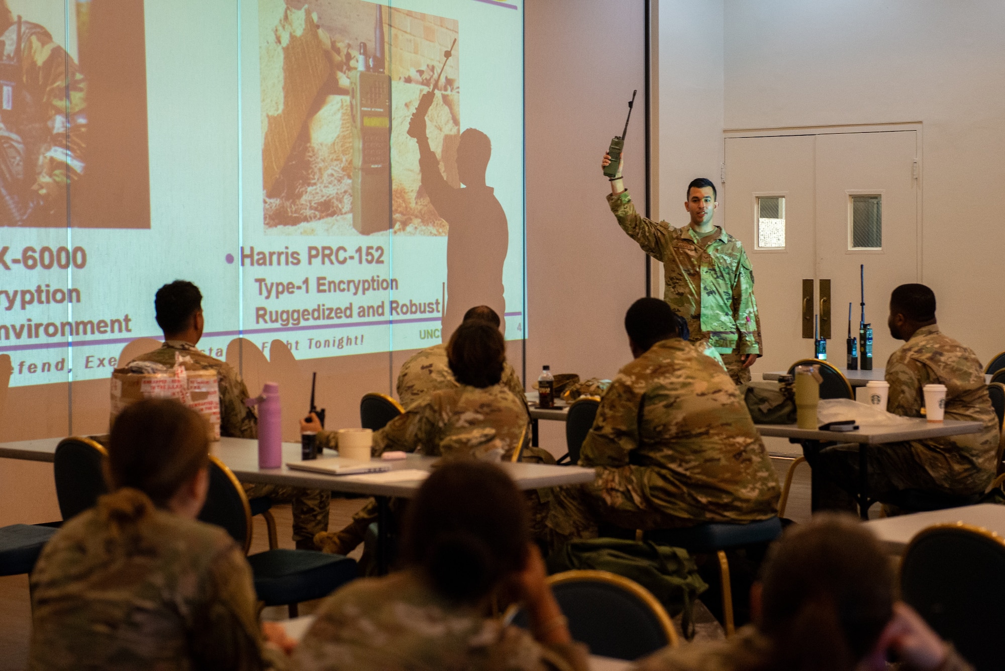 An Airman holds up a radio while briefing its capabilities.