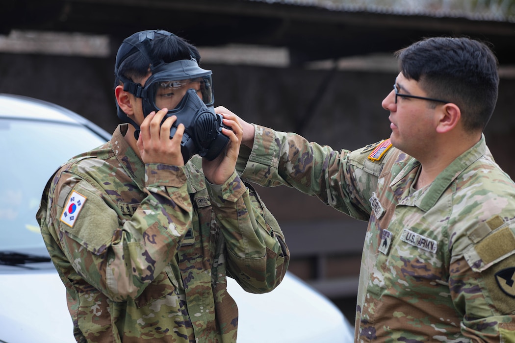 U.S. Army Sgt. Remi Torres, assigned to Headquarters and Headquarters Company, U.S. Army Garrison Yongsan-Casey, helps Korean Augmentation to the U.S. Army Pfc. Hyun Jae Chung don his promask before a gas chamber drill at North Star Range, Uijeongbu, South Korea, March 5, 2025.