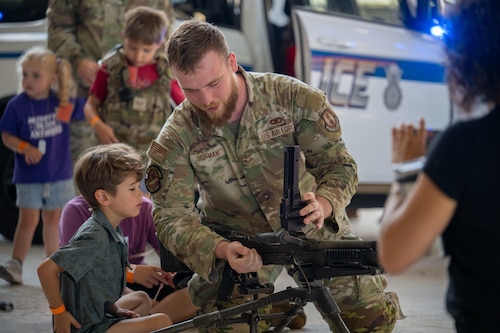 Senior Airman Dakota Hoffman, of the 88th Security Forces Squadron, demonstrates an M240B machine gun for a child during the Kids Understanding Deployment Operations (KUDOS) event Aug. 8, 2025, at Wright-Patterson Air Force Base, Ohio. KUDOS teaches children about deployments and weapons safety. (U.S. Air Force photo by Jack Gardner)