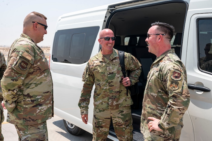 Chief Flosi in the middle of frame laughs as he looks to Col. Shanks right of frame in front of a van with Col. Stouffer left of frame