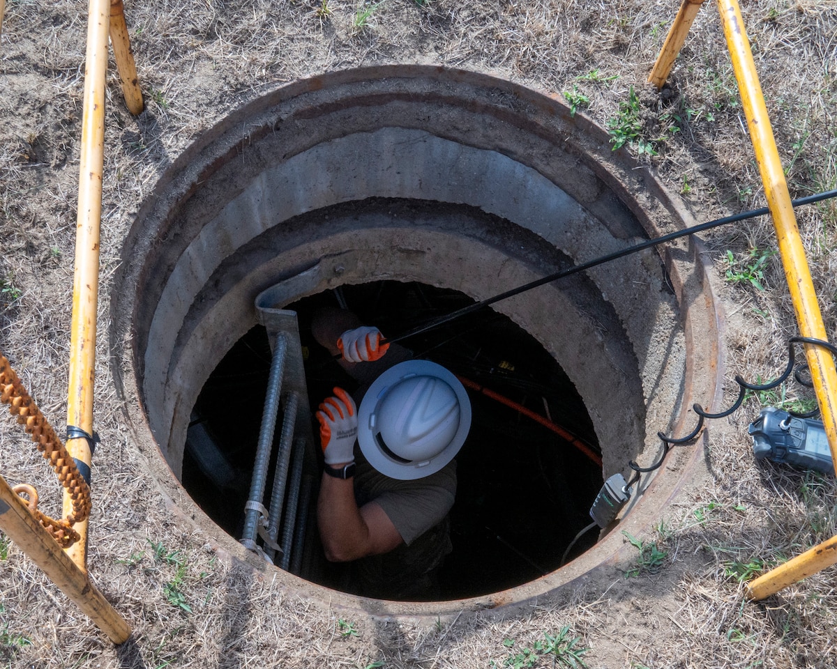 Tech. Sgt. Benjamin Dutting, 212th Engineering Installation Squadron cable and antenna technician, feeds fiber optic cable through a communications conduit during an infrastructure upgrade on Otis Air National Guard Base, Mass., Aug. 8, 2025. Members of the 212th EIS performed a critical communications infrastructure upgrade while simultaneously performing hands-on training and qualification. (U.S. Air National Guard photo by Timothy Sandland)