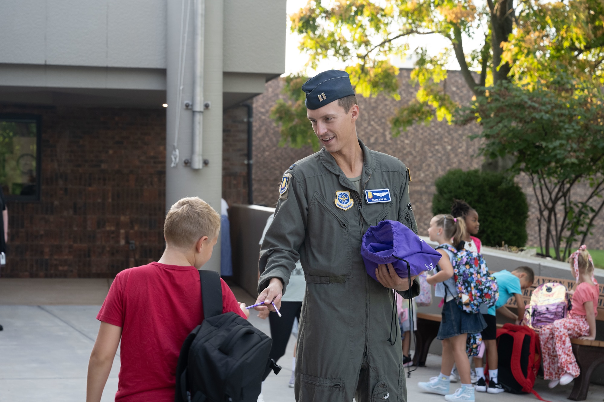Capt. William Bowling, 350th Air Refueling Wing pilot, hands a pencil to a student at Tanglewood Elementary School, Derby, Kansas, Aug. 14, 2025. As part of the Fist Bumps and High Fives program, Bowling greeted students as they walked into school. (U.S. Air Force photo by Senior Airman Felicia Przydzial)