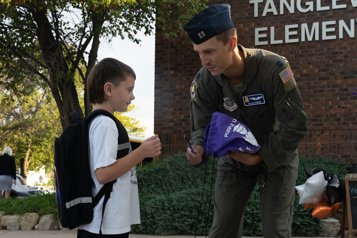 Capt. William Bowling, 350th Air Refueling Wing pilot, hands a pencil to a student at Tanglewood Elementary School, Derby, Kansas, Aug. 14, 2025. This year, Airmen were volunteered to greet students at seven different schools in the local area. (U.S. Air Force photo by Senior Airman Felicia Przydzial)